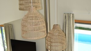 Un salon moderne doté d’un téléviseur à écran plat, de luminaires suspendus en osier, d’un meuble de rangement blanc et offrant une vue sur l’océan grâce à de grandes fenêtres.