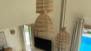 Un salon spacieux doté d’un téléviseur à écran plat, de lampes en osier, d’une cheminée et offrant une vue sur une piscine.