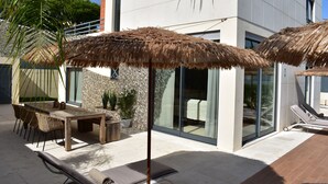 Une terrasse extérieure moderne, dotée d’une table à manger, de chaises et de deux parasols à toits de chaume.