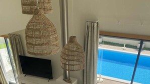 Un salon moderne avec une télévision, des lampes en osier, un canapé et une vue sur une piscine.