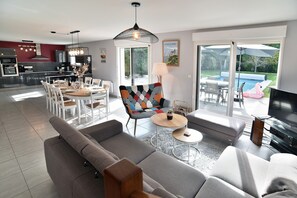 A modern living space with a dining area, a sofa set, a TV, and a poolside view. - Les 9 plages - Piscine privée (Saint-Briac-sur-Mer)