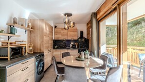 A modern kitchen with wooden cabinets, a built-in oven, and a dining area with grey chairs. - L'Etoile du Roc - Au pied du Roc D'Enfer (Saint-Jean-d'Aulps)