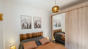 A bedroom with a wooden headboard, a large bed with a quilted cover, two wall-mounted paintings, a bedside lamp, and a hanging light fixture. - L'Etoile du Roc - Au pied du Roc D'Enfer (Saint-Jean-d'Aulps)