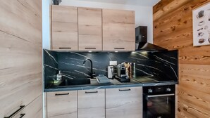 A modern kitchen with wooden cabinets, a black marble countertop, and a built-in oven. - L'Etoile du Roc - Au pied du Roc D'Enfer (Saint-Jean-d'Aulps)