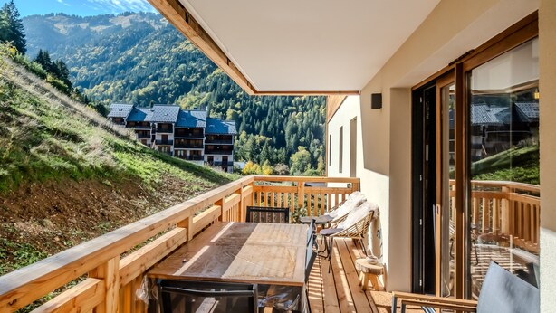 A wooden deck with a table and chairs, overlooking a mountainous landscape with buildings. - L'Etoile du Roc - Au pied du Roc D'Enfer (Saint-Jean-d'Aulps)