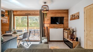 A modern cabin interior with a dining area, sofa, and a TV mounted on the wall. - L'Etoile du Roc - Au pied du Roc D'Enfer (Saint-Jean-d'Aulps)