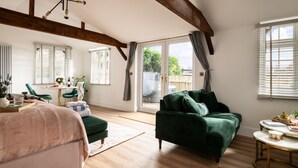A spacious living room with a green sofa, a pink armchair, and a wooden ceiling. - Stargazing Studio with Private Hot Tub (Blandford Forum)