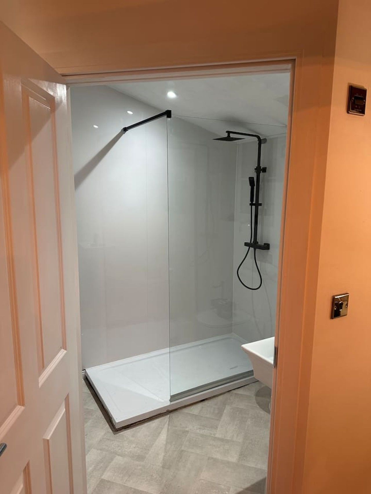 Une salle de bain moderne avec une douche à parois de verre, un lavabo blanc et un sol carrelé.