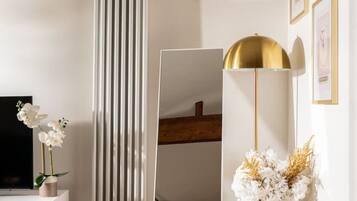 A room with a white radiator, a large mirror, a television, a wooden cabinet, and a vase with flowers.