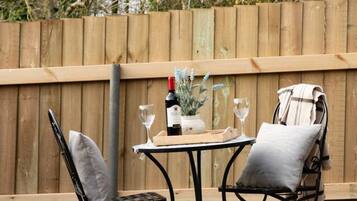 An outdoor seating area with a table and two chairs, a bottle of wine, and a vase with flowers.
