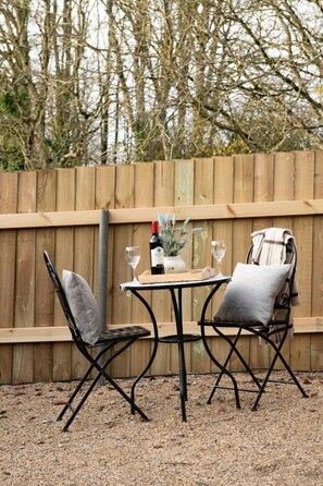 Un espacio de estar al aire libre con una mesa y dos sillas, una botella de vino y un jarrón con flores.