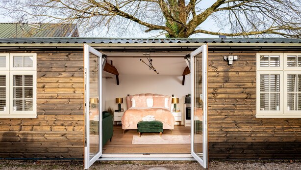 A wooden cabin with a bedroom featuring a bed, bedside tables, and a green bench. - Stargazing Studio with Private Hot Tub (Blandford Forum)