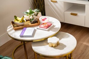 Een ronde tafel met een boek, een schaal met bananen, een vaas met bloemen en een klein witte bakje.