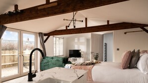 A bedroom with a large bed, a bathroom with a sink, and a TV in the background. - Stargazing Studio with Private Hot Tub (Blandford Forum)