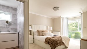 Un dormitorio con una cama grande, mesitas de noche, una ventana y vistas al verdor exterior.