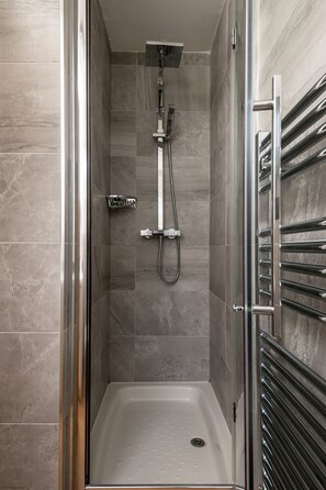 Une douche à l’italienne avec une porte en verre, une douchette à main et un porte-serviettes chromé.