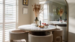 Un comedor con una mesa redonda, sillas, un jarrón con plantas secas y un espejo grande.