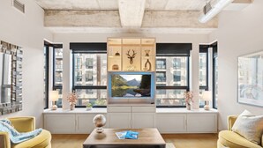 Un salon moderne doté d’un grand téléviseur, d’étagères intégrées et de grandes fenêtres offrant une vue sur la ville.