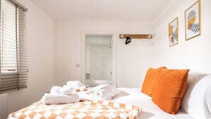 Une chambre d’hôtel avec un lit, une couverture à carreaux, un oreiller orange et une porte donnant sur une salle de bain.