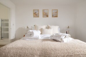 A neatly made bed with rolled towels, a white textured bedspread, and three framed artworks on the wall.