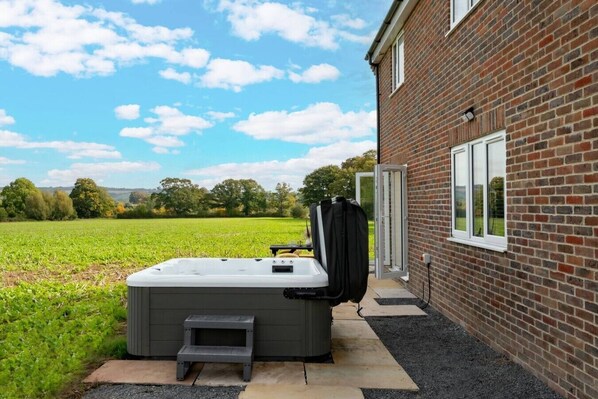 A hot tub outside a brick building with a clear sky and a green field in the background.