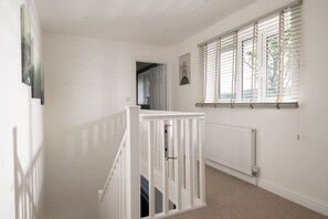 A hallway with a white railing, a radiator, and a window with blinds. - Hambledon Hill Cottage with Private Hot Tub (Blandford Forum)