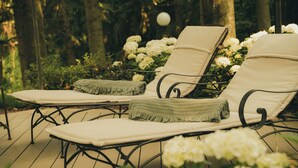 Two lounge chairs with cushions on a wooden deck, surrounded by white flowers and greenery. - Suite Percalle (Castelvetro di Modena)