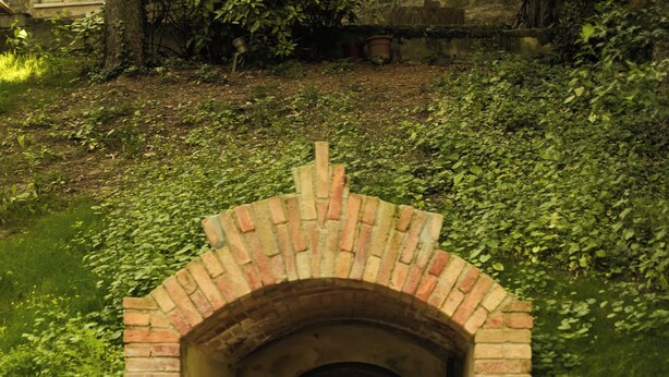 A brick tunnel with a gravel path leading into it, surrounded by greenery. - Suite Percalle (Castelvetro di Modena)