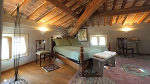 A bedroom with a wooden ceiling, a bed, a chair, a desk, and a floor lamp. - Suite Percalle (Castelvetro di Modena)