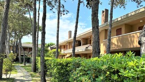 A pathway leading to a building with multiple balconies and a garden area with trees and shrubs.