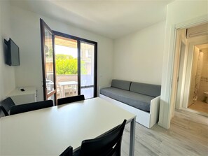 En kompakt opholdsstue med spisebord, sofa og en skydedør, der fører til et udendørs område med bord og stole.