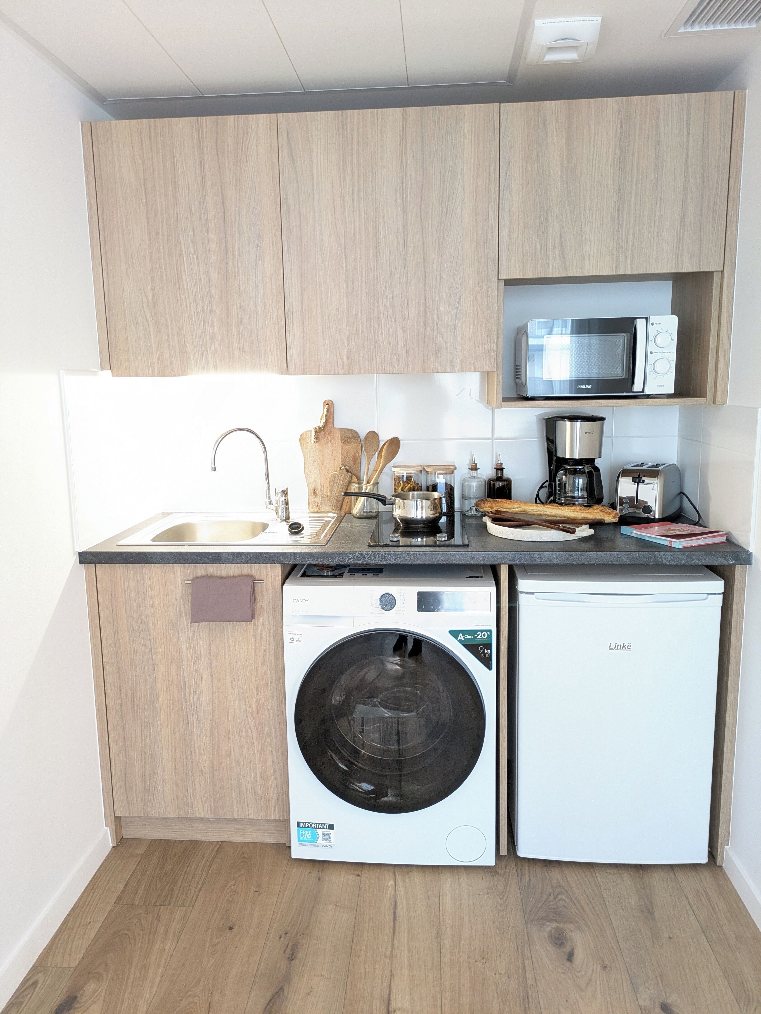 A compact kitchen with a washing machine, dishwasher, microwave, and a coffee maker.