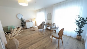 Un salon moderne comprenant un coin repas, un plancher en bois et une grande fenêtre agrémentée de rideaux légers.