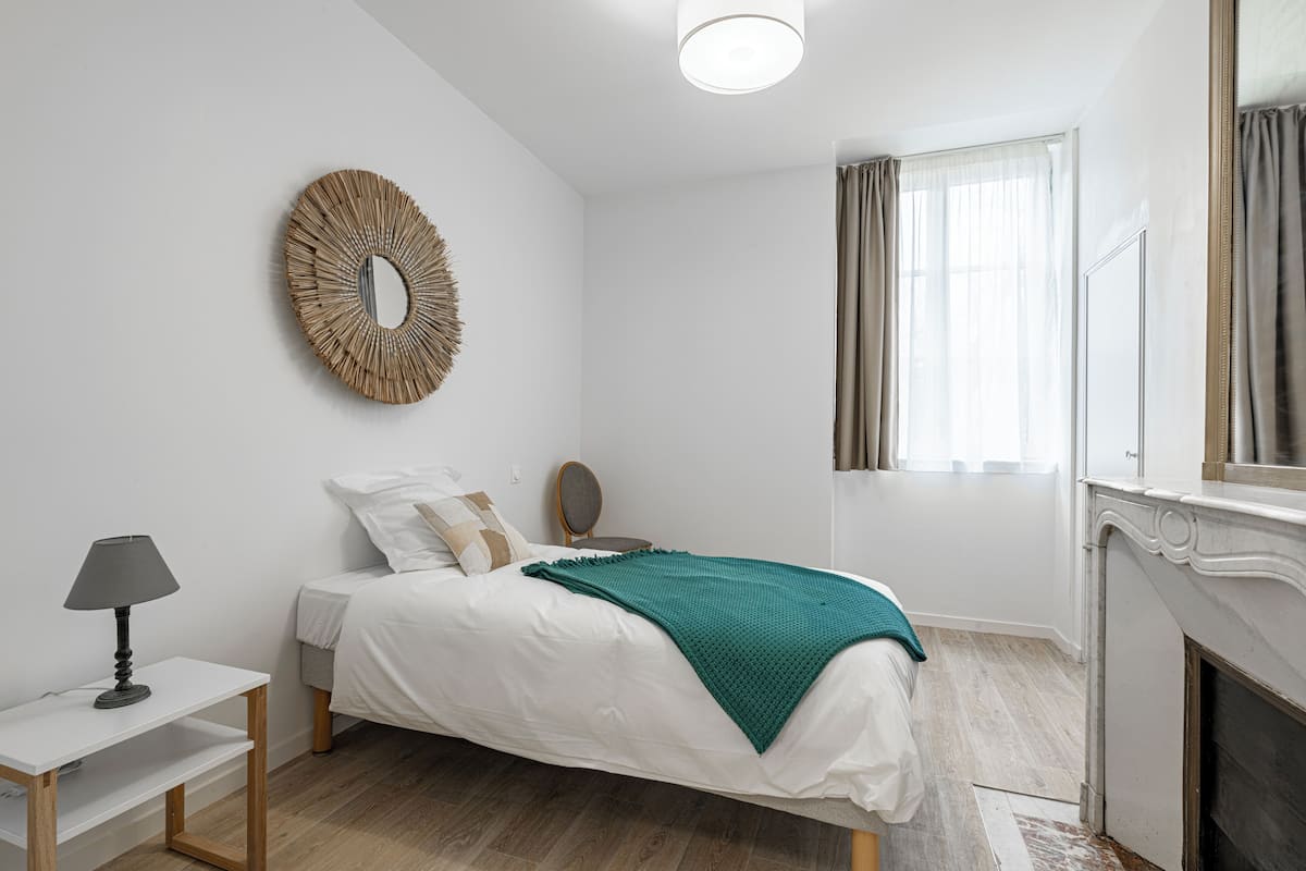A bedroom with a bed, bedside table, lamp, mirror, and a fireplace.