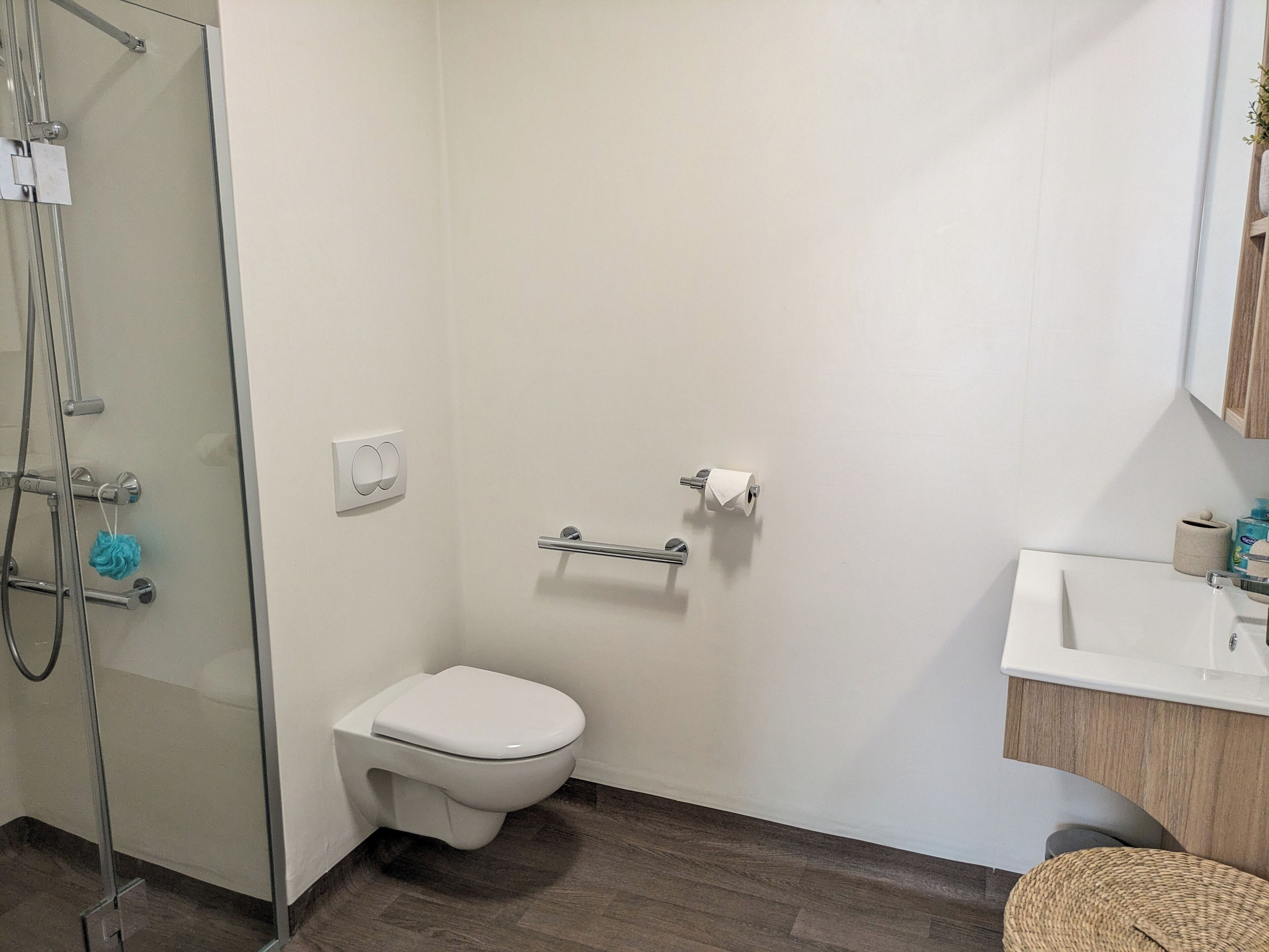 Un baño moderno con cabina de ducha de vidrio, inodoro blanco y tocador de madera con lavabo.