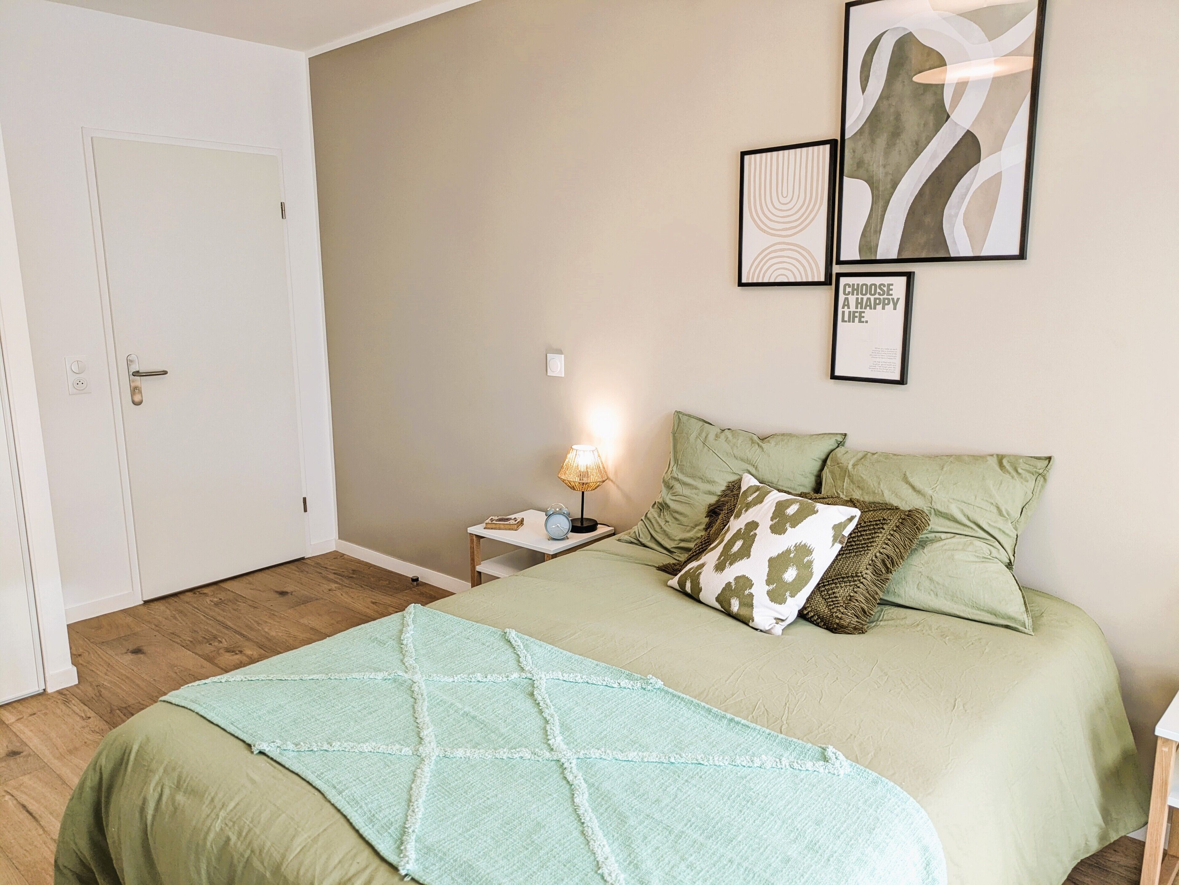 A bedroom with a bed, a bedside table with a lamp, and wall art.