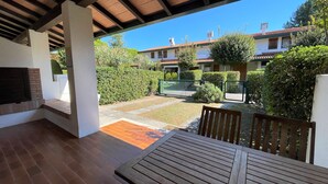 Une terrasse couverte avec une table et des bancs en bois, une cheminée en briques et une vue sur un quartier résidentiel avec des maisons et de la verdure.