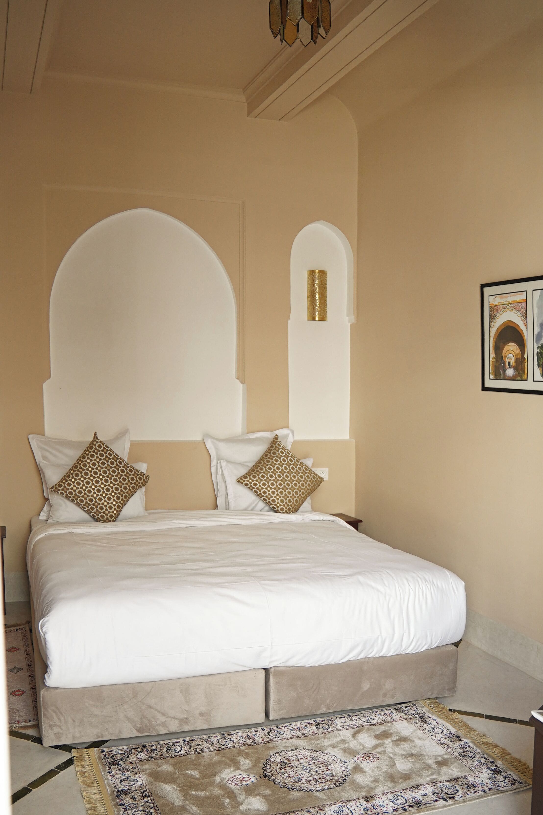 A bedroom with a large bed, two pillows, a headboard, a nightstand, and a patterned rug.
