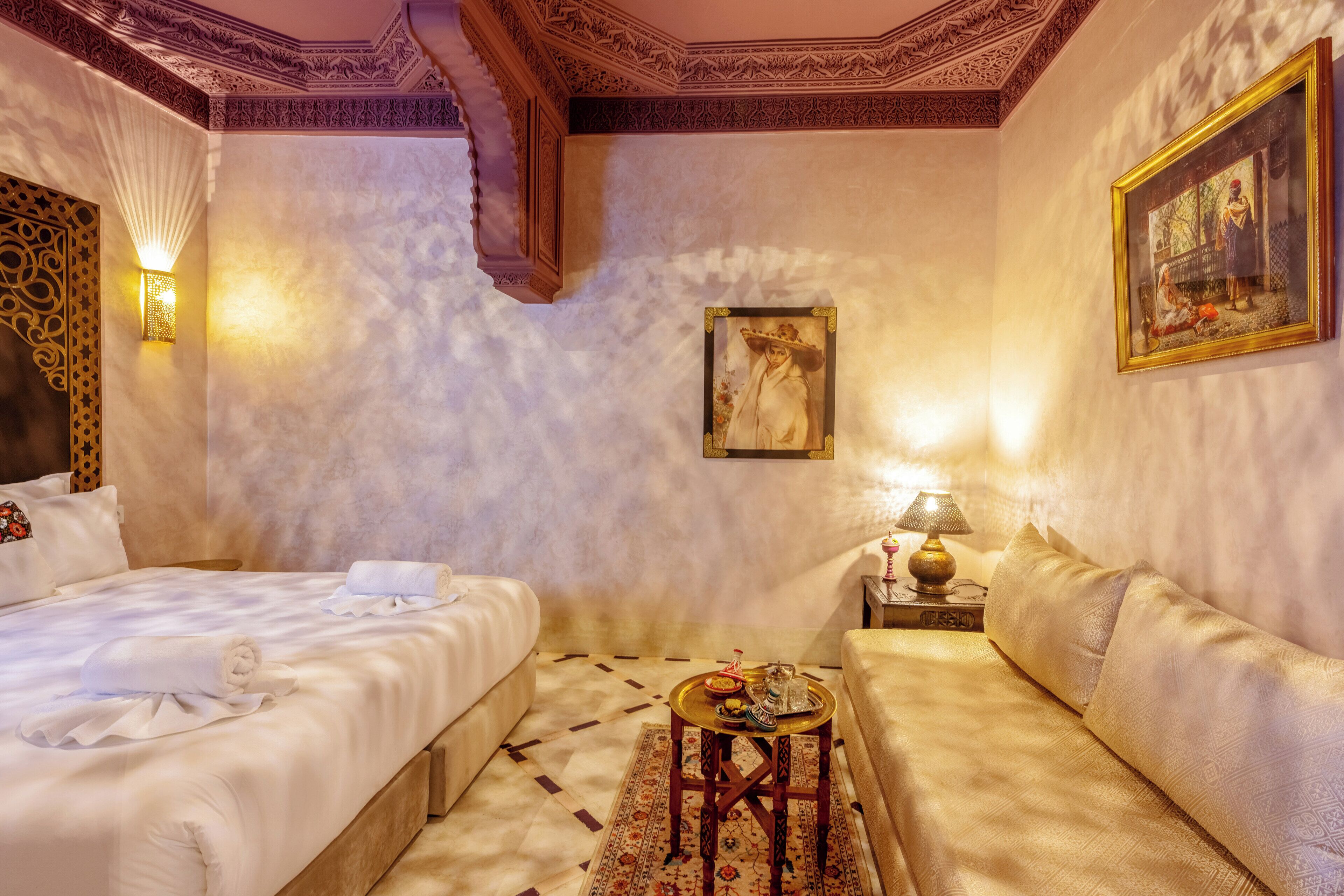 A hotel room with a large bed, a sofa, a small table with a lamp, and a painting on the wall.