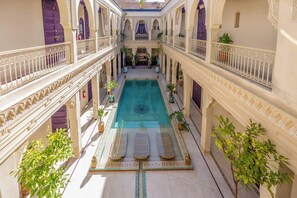 A courtyard with a central pool, ornate railings, and potted plants.