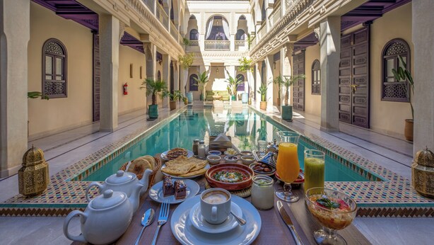 A poolside breakfast setup with a variety of foods and drinks, surrounded by ornate architecture. - Palais Andara Riad And SPA (Marrakech)