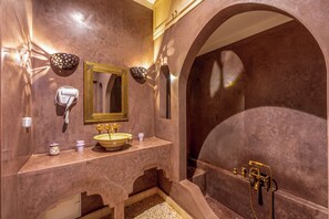 A bathroom with a marble vanity, a gold-framed mirror, a sink with a bowl, and a bathtub with a showerhead.