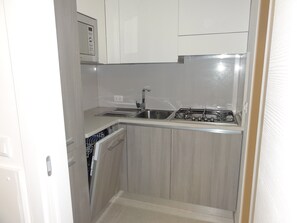 A compact kitchen with a built-in microwave, a sink, and a stove. - Charming Renovated Flat (San Michele al Tagliamento)