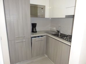 Cocina compacta equipada con microondas, cafetera, lavavajillas y estufa a gas.