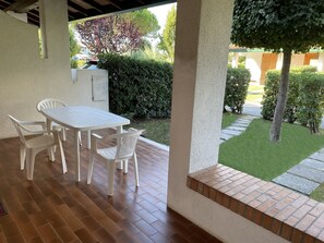 A patio with a white table and chairs, a brick floor, and a view of a garden with a tree and bushes. - Bright Two-storey Flat (San Michele al Tagliamento)