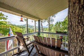 Un área de estar al aire libre con techo, con sillas y mesas de madera, con vistas a un paisaje pintoresco con árboles y montañas.