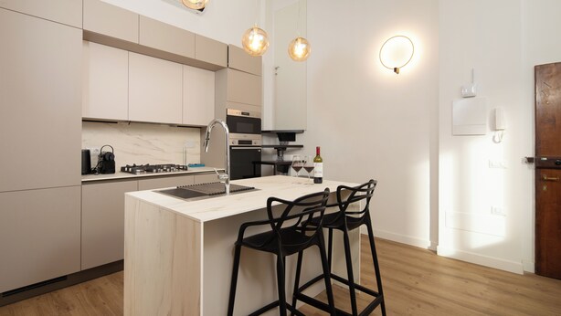 Une cuisine moderne dotée d’un îlot central, de tabourets de bar, de luminaires suspendus et d’un four encastré.