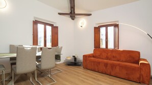 Un salon moderne avec un plafond en bois, un canapé, une table à manger avec des chaises et deux fenêtres avec des rideaux.