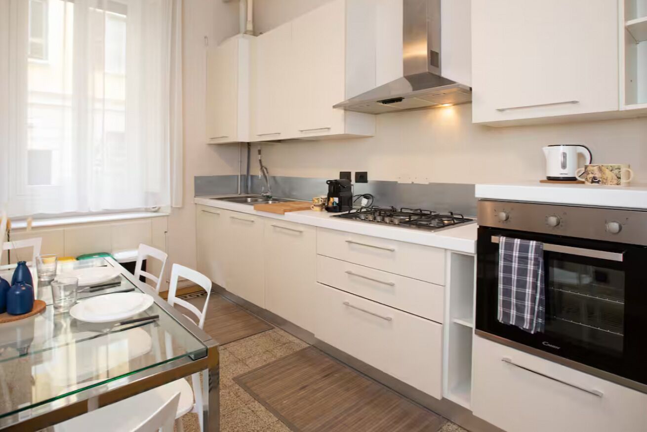 Een moderne keuken met witte kastjes, een gasfornuis, een oven en een raam met dunne gordijnen.
