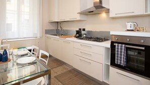Eine moderne Küche mit weißen Schränken, einem Gasherd, einem Backofen und einem Fenster mit durchsichtigen Vorhängen.